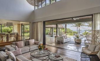 a spacious living room with large windows offering views of the ocean and palm trees , featuring a comfortable couch and coffee table at Four Seasons Resort Mauritius at Anahita