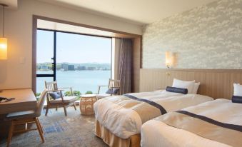 a modern hotel room with two beds , wooden furniture , and a large window offering a view of the water at Hotel Ichibata