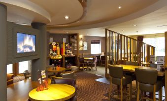 a hotel lobby with a bar , dining area , and arcade game machines , creating a lively atmosphere at Premier Inn Burgess Hill