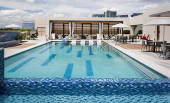 a large swimming pool with blue tiles is surrounded by white lounge chairs and umbrellas , overlooking a building at Renaissance Dallas at Plano Legacy West Hotel