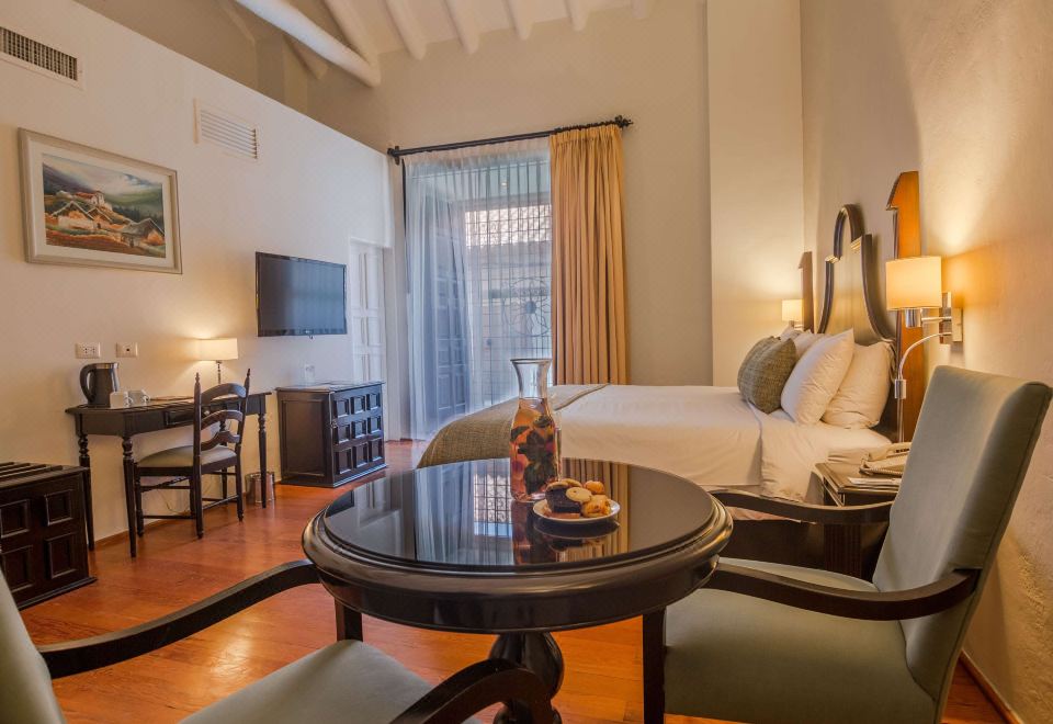 a well - decorated hotel room with a comfortable bed , a television , and a dining table at Novotel Cusco