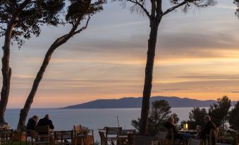 a serene sunset view from a beach , with people sitting at tables under trees and enjoying the view at Boutique Hotel Torre di Cala Piccola