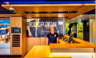 a hotel lobby with a wooden reception desk and a man standing behind it , wearing a mask at Ibis Budget Windsor Brisbane