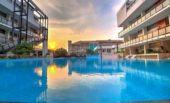 an outdoor swimming pool surrounded by multiple buildings , with the sun setting in the background at Hotel Somadevi Angkor Resort & Spa