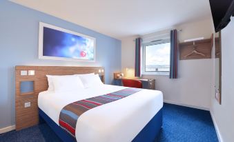 a large bed with a blue and red headboard is in the middle of a room with a window , framed picture , and a window at Travelodge Southport