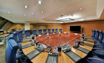 a large conference room with a wooden table , multiple chairs , and a large screen at the front at Transcorp Hilton Abuja