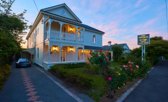 a large white house with a balcony , surrounded by lush greenery and flowers , at dusk at Windarra on High
