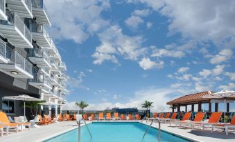 a large swimming pool with orange lounge chairs and a hotel building in the background at Aloft Ocean City