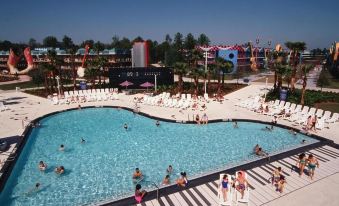 a large outdoor swimming pool surrounded by multiple buildings , with people enjoying their time in the water at Disney's All-Star Music Resort