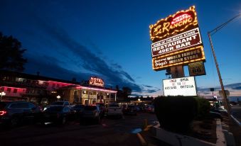 a neon sign for a restaurant and bar is lit up at night , with cars parked outside at Hotel El Rancho