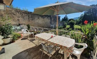 a patio with a dining table , chairs , and an umbrella is shown in front of a stone wall at Chez Pierre