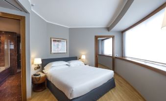 a large , neatly made bed with white linens is in a room with wooden floors and gray walls at B&B Hotel Trapani Crystal