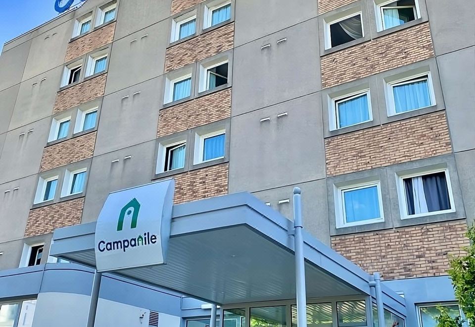 "a modern building with a green sign that reads "" campanile "" and large windows , under a clear blue sky" at Campanile Paris Est - Bobigny