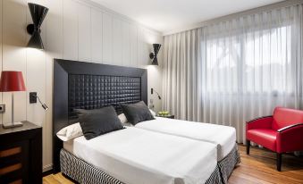 a modern bedroom with a black headboard , white bedding , and red chair in the corner at Salles Hotel Aeroport de Girona