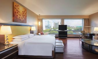 a modern hotel room with wooden floors , white bedding , and large windows offering a view of the city at Courtyard by Marriott Mumbai International Airport