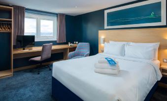 a modern hotel room with a white bed , blue walls , and a desk with a computer at Travelodge Leatherhead
