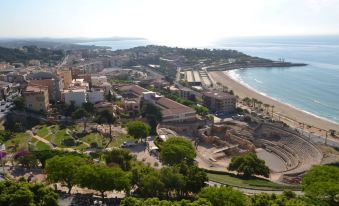 a cityscape with a beach in the foreground and buildings in the background , along with trees and sand at H10 Imperial Tarraco