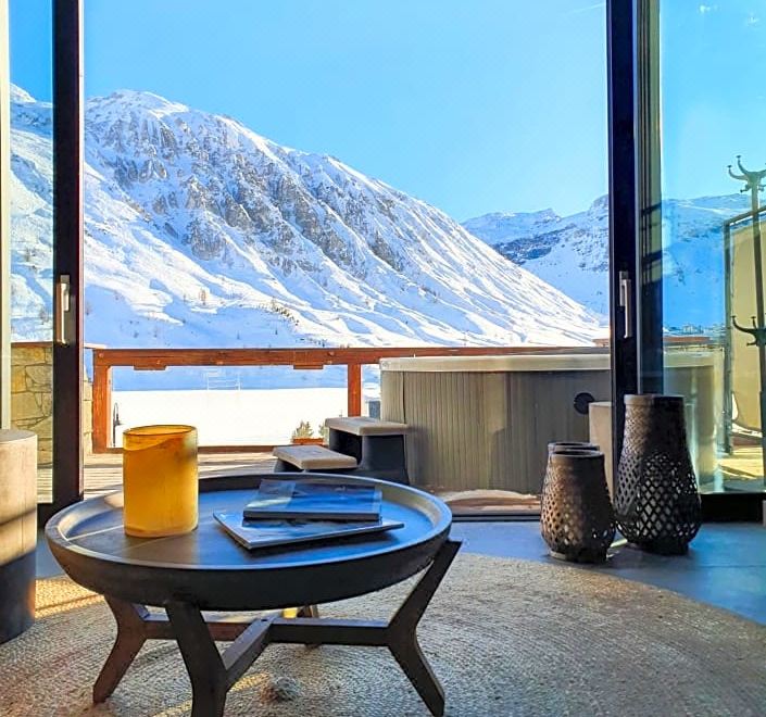 a balcony with a table , chairs , and a cup of tea is shown with a snowy mountain view at Langley Hotel Tignes 2100