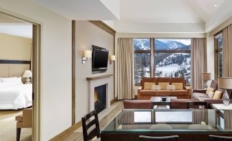 a spacious living room with a large window overlooking a snowy mountain view , featuring a dining table and chairs , a couch , and a television at The Westin Riverfront Resort & Spa, Avon, Vail Valley