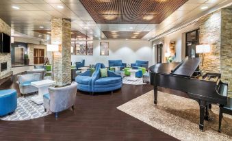 a spacious living room with blue couches , chairs , and a black grand piano in the center at The Mosey Buffalo Williamsville, Tapestry Collection by Hilton
