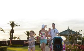 a family of four is walking down a path in a park , with one adult pushing a stroller and two children at Sea World Resort