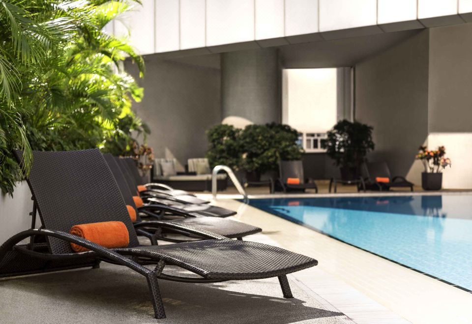 An outdoor seating area with lounge chairs and tables is located next to the swimming pool at Novotel Century Hong Kong