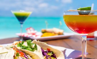 a table with two plates of tacos and a drink , with the ocean visible in the background at Pelican Beach Hotel