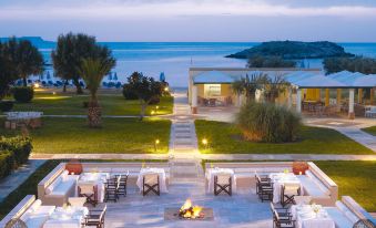 an outdoor dining area with tables and chairs , surrounded by a large body of water at Grecotel Meli Palace