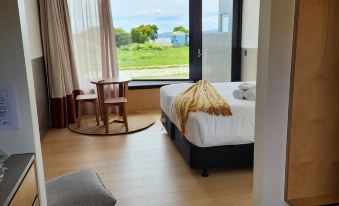 a hotel room with a large window overlooking the ocean , featuring a bed , a chair , and a dining table at Bruny Island Escapes and Hotel Bruny