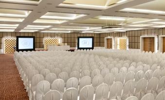 a large , empty conference room with rows of white chairs and two televisions on either side at Hyatt Centric Janakpuri New Delhi
