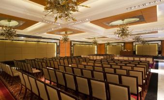 a large , well - lit conference room with rows of chairs arranged in front of a long table at Taj Club House