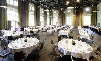 a large banquet hall filled with round tables and chairs , ready for a formal event at Steigenberger Braunschweig