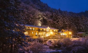 a snow - covered mountainous area with a large building , lit up at night , surrounded by trees and trees at Shima Onsen Kashiwaya Ryokan