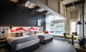a modern hotel room with two beds , a desk , and a window , decorated with red artwork at Ovolo Woolloomooloo