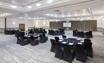 a large conference room with rows of tables and chairs , a screen at the front , and a podium at DoubleTree by Hilton Swindon