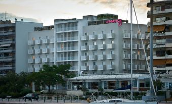 a white building with a pink sign and balconies is surrounded by boats and trees at Moxy Patra Marina