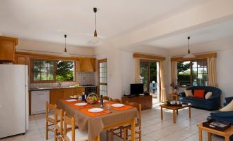 a dining table with a plate of food and chairs is set in a spacious living room at Panareti Coral Bay Resort