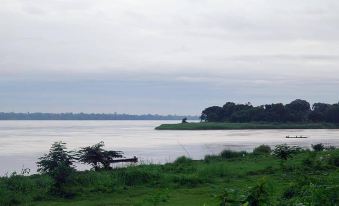 a serene landscape of a river , with a boat floating on the water and lush greenery surrounding it at Baan Rim Khong Resort