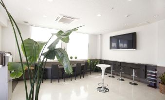 a modern office space with white walls , black furniture , and green plants , as well as a large screen on the wall at Toyota Village