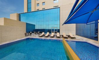 an outdoor swimming pool surrounded by a hotel , with several lounge chairs and umbrellas placed around the pool area at Hilton Garden Inn Tabuk