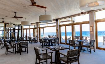 a modern , open - air restaurant with wooden floors and large windows offering views of the ocean at Kagi Maldives Resort & Spa
