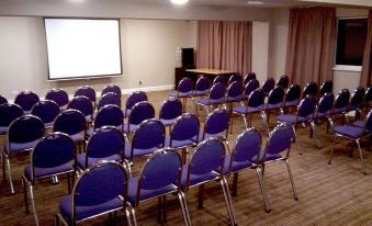 a conference room with rows of blue chairs arranged in a semicircle , and a projector screen on the wall at Skylark Hotel