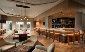 a modern , well - lit bar with wooden floors and chairs , along with a bar area featuring a wine rack at Embassy Suites by Hilton Monterey Bay Seaside