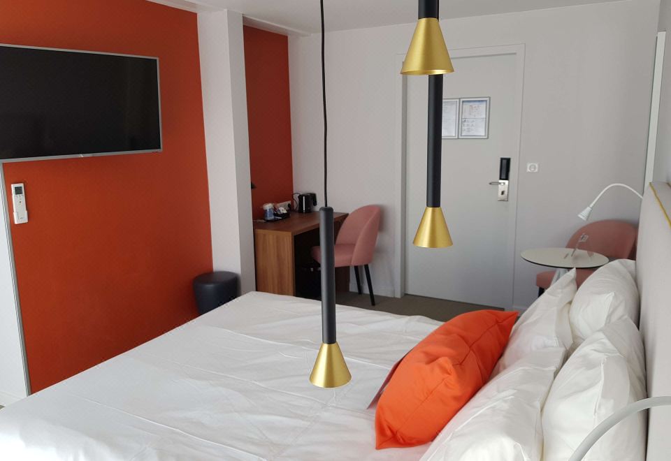 a hotel room with a bed , desk , and chairs , as well as an orange accent wall at Kyriad Lyon Est - Saint Quentin Fallavier