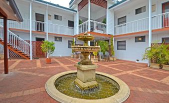 a courtyard with a fountain surrounded by multiple buildings , including a white building with balconies and green trees at Dolphin Lodge Albany - Self Contained Apartments at Middleton Beach