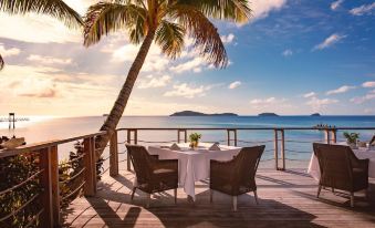 a wooden deck overlooking the ocean , with a dining table and chairs set up for a meal at Kokomo Private Island Fiji