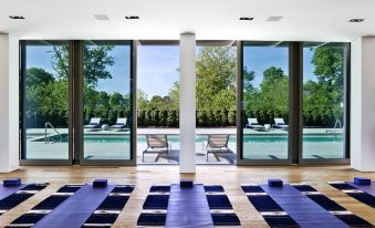 a room with a long window and several yoga mats on the floor , surrounded by chairs and a pool in the background at Topping Rose House