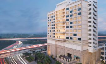 a large white hotel with a tall building and several cars driving on the road at Crowne Plaza New Delhi Mayur Vihar Noida