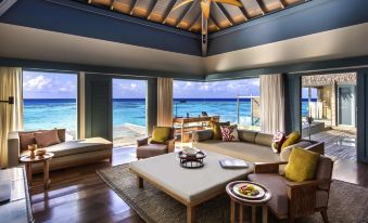 a spacious living room with a view of the ocean , featuring a large flat - screen tv mounted on the wall at Raffles Maldives Meradhoo Resort