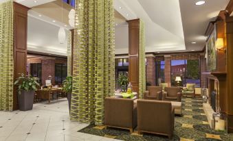 a large , well - lit hotel lobby with multiple seating areas , including couches , chairs , and a dining table at Hilton Garden Inn Bartlesville
